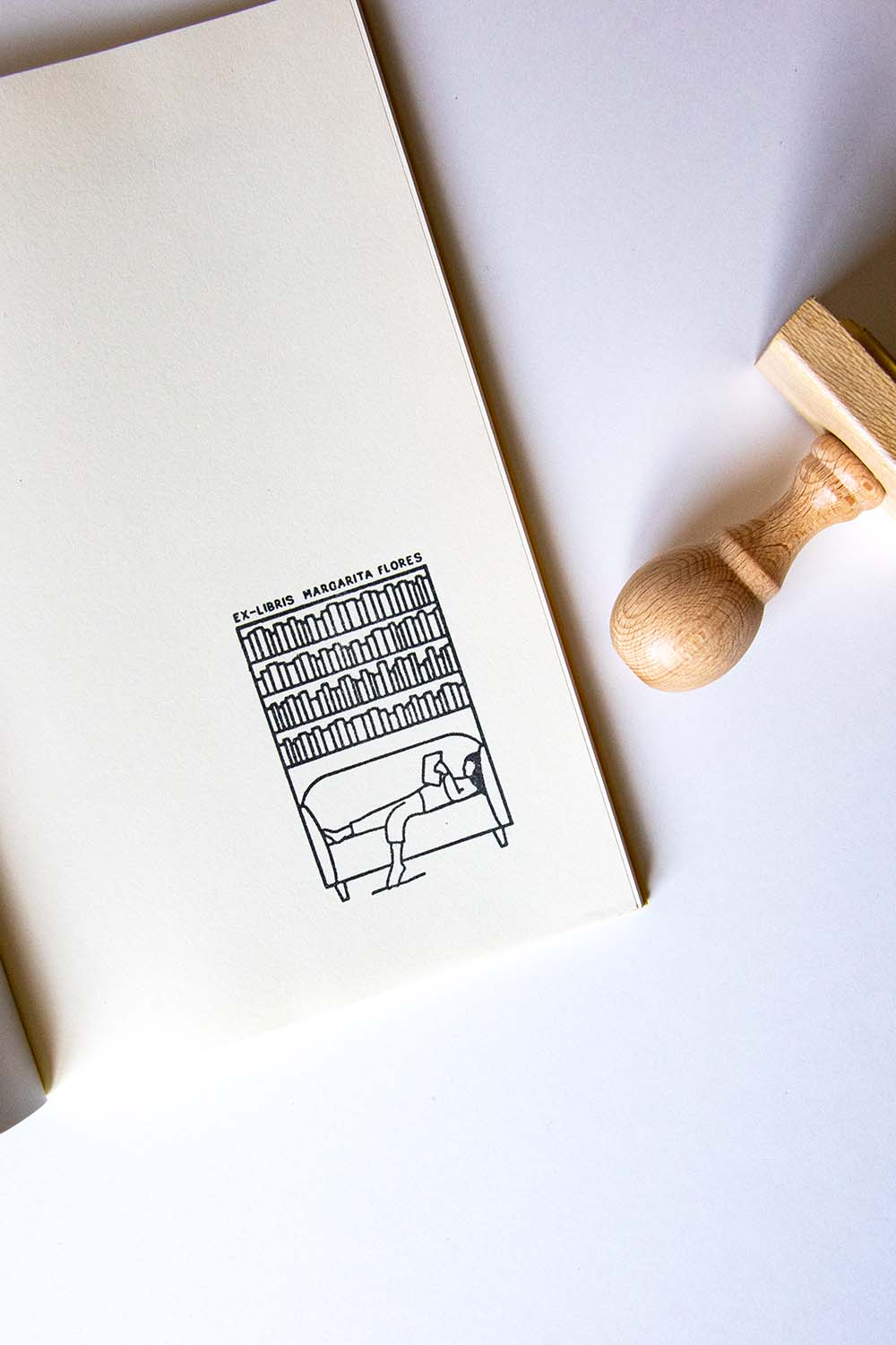 Portadilla de libro estampada con una chica estirada leyendo en un sofa y una biblioteca detrás y sello