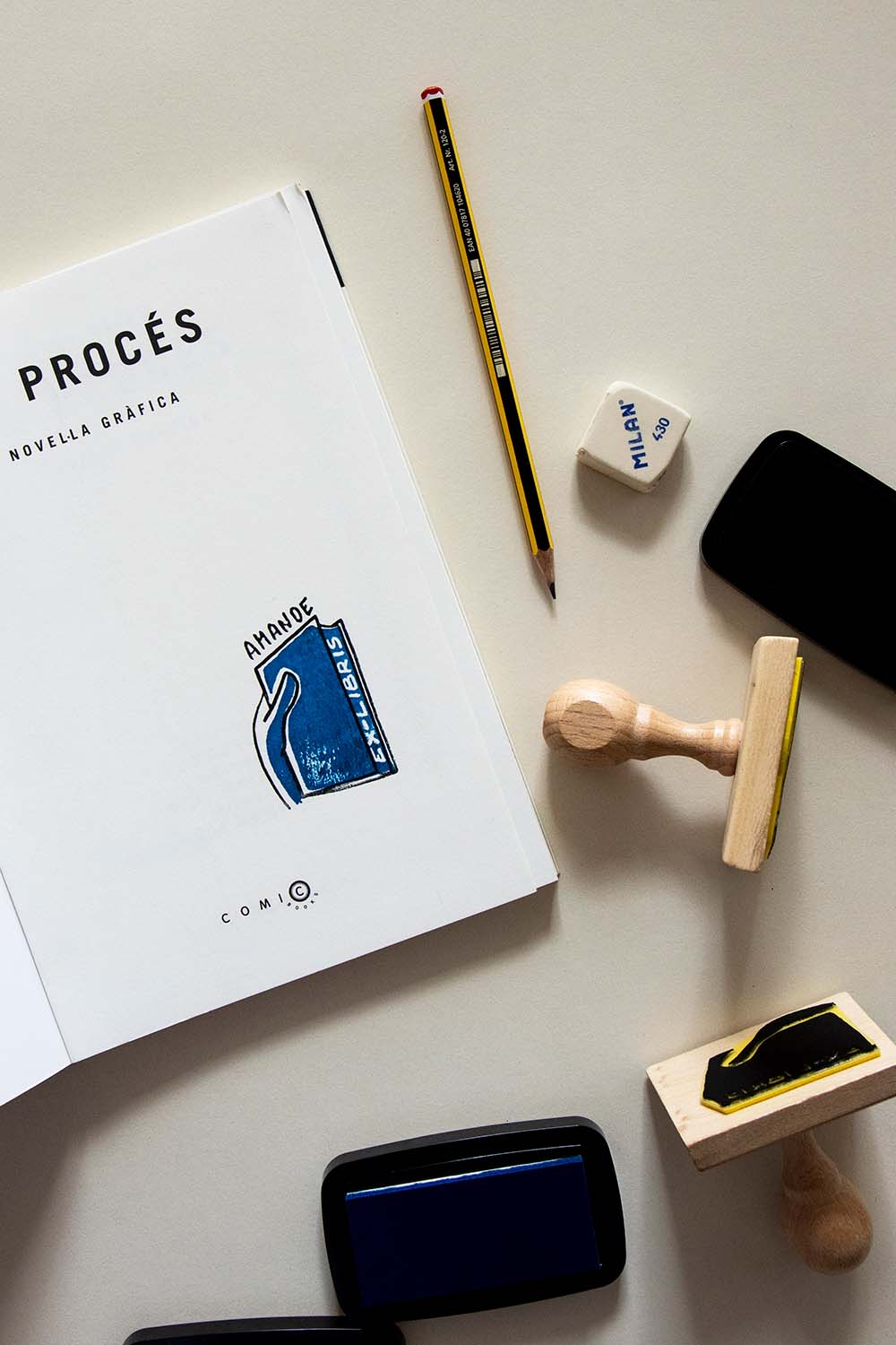 Portadilla de libro estampada con un sello exlibris de una mano cogiendo un libro azul y sellos