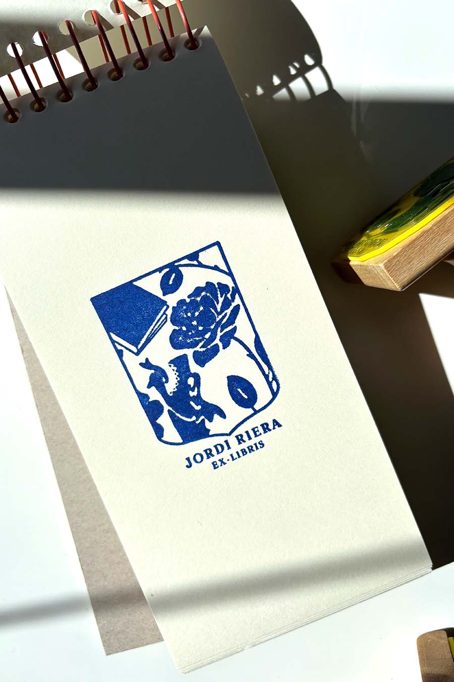 Portadilla de libro estampada con sello exlibris de un escudo con una rosa, un libro y un dragón y sello