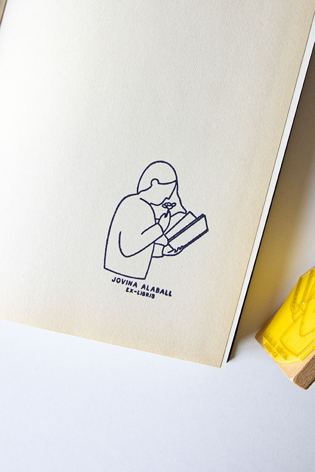 Portadilla de libro estampada con una lectora leyendo y oliendo una rosa