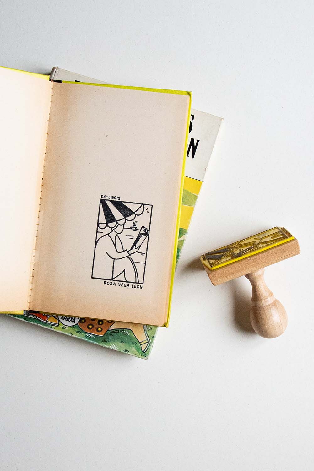 Portadilla de un libro estampada con una persona leyendo bajo la sombrilla en la playa y sello