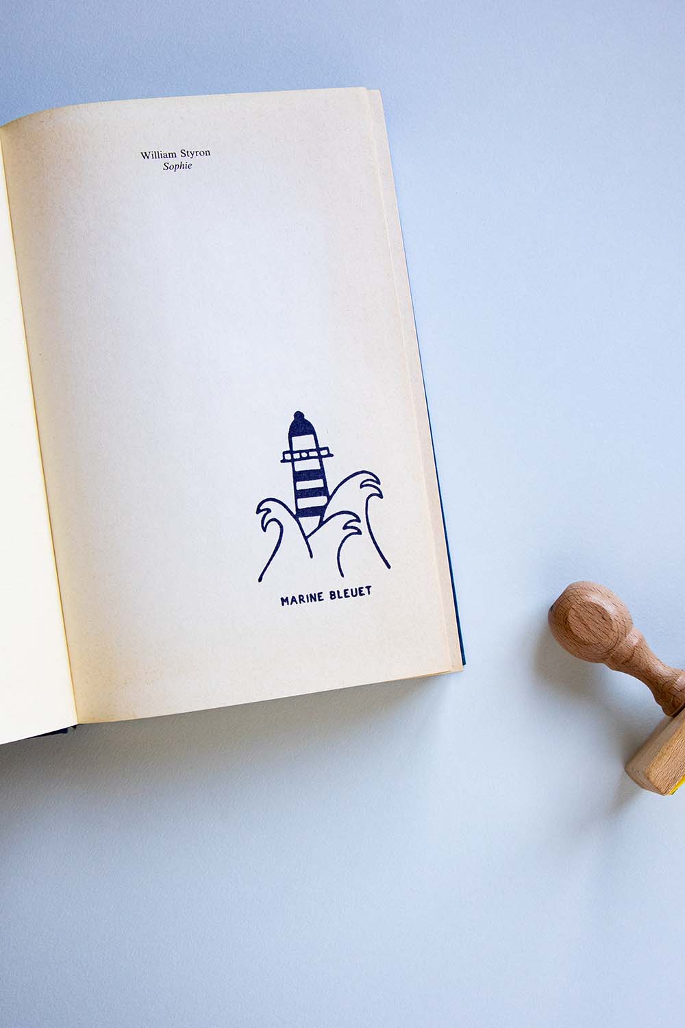 Portadilla de un libro estampada con un faro entre olas y sello