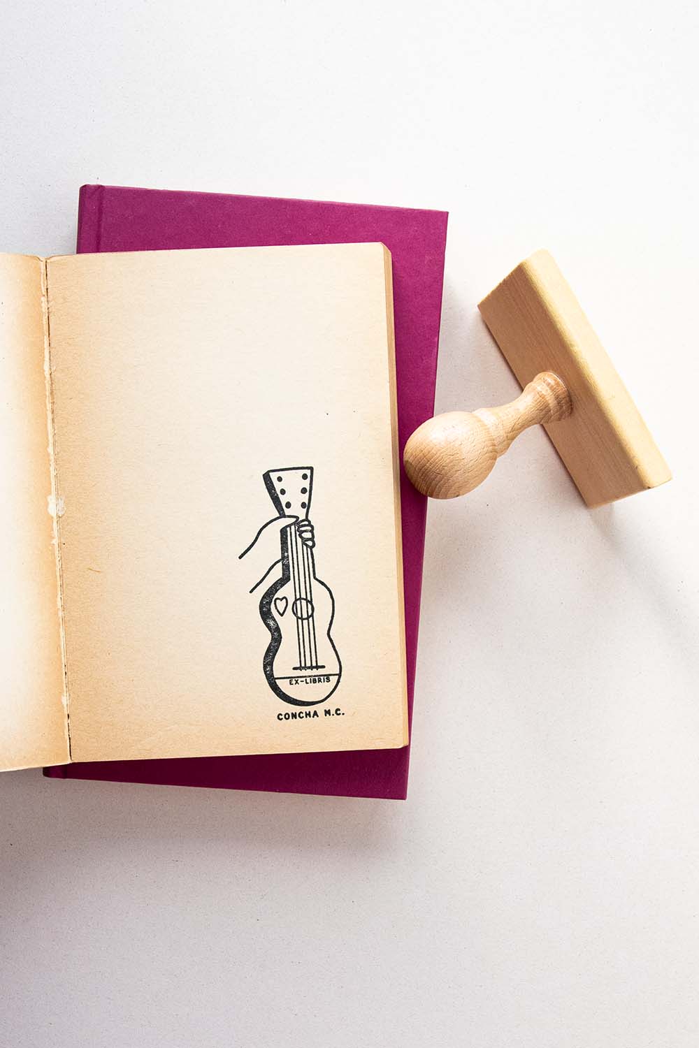 Portadilla de libro estampada con sello exlibris de una mano sosteniendo una guitarra y sello