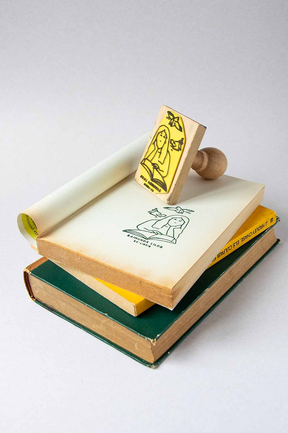 Sello exlibris grabado con una mujer leyendo un libro, con dos libros volando sobre ella
