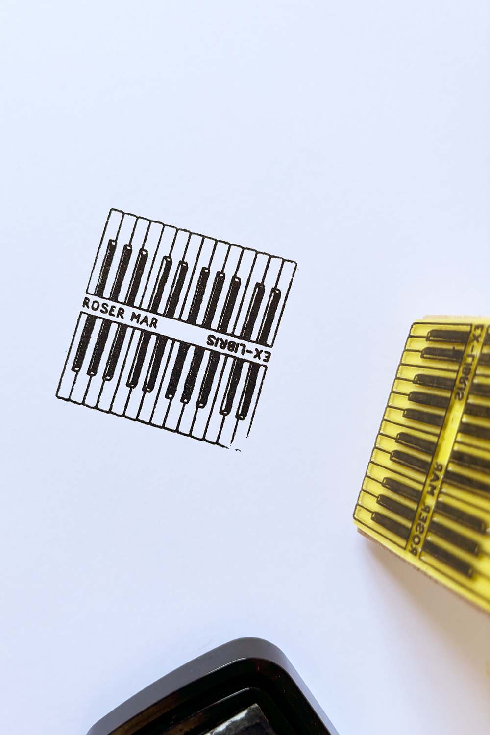 Portadilla de libro estampado con sello exlibris de dos teclados de piano y sello