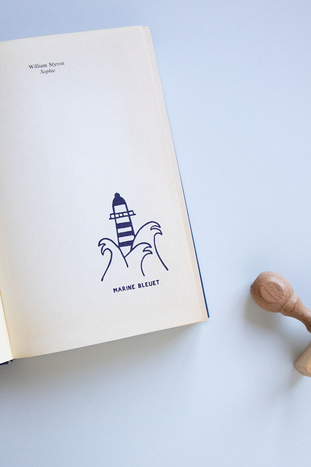 Portadilla de un libro estampada con un faro entre olas y sello