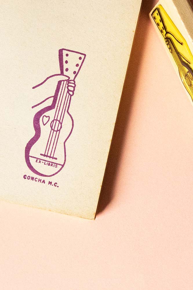 Portadilla de libro estampada con sello exlibris de una mano sosteniendo una guitarra